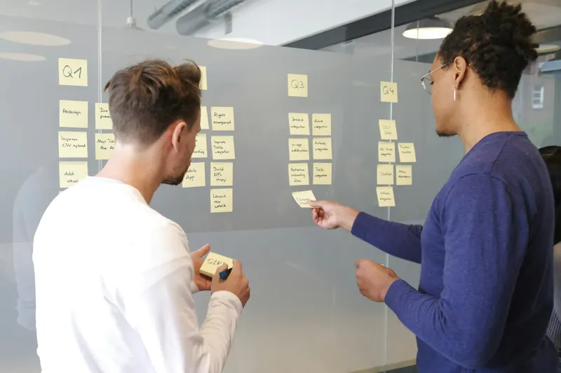 Two colleagues arranging sticky notes on a glass wall during a planning session