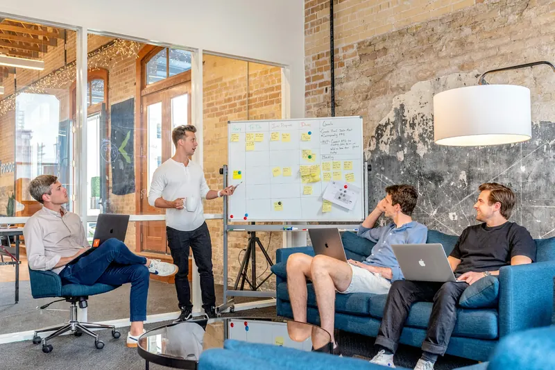 A speaker presenting to a seated team in a bright brick-walled workspace