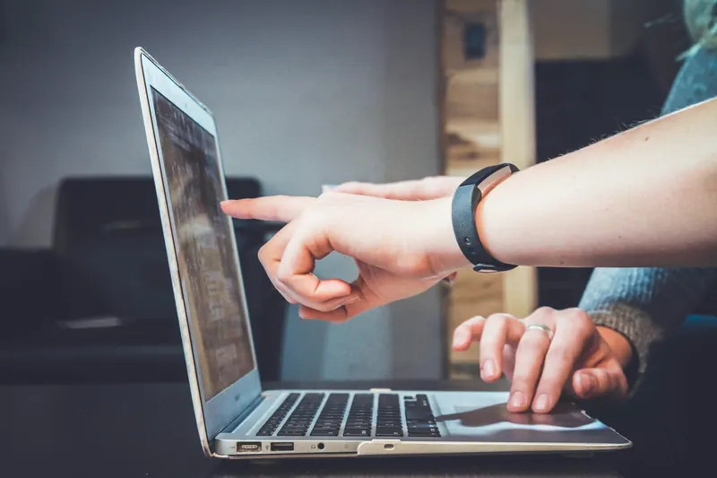A colleague pointing at a laptop screen while reviewing a report