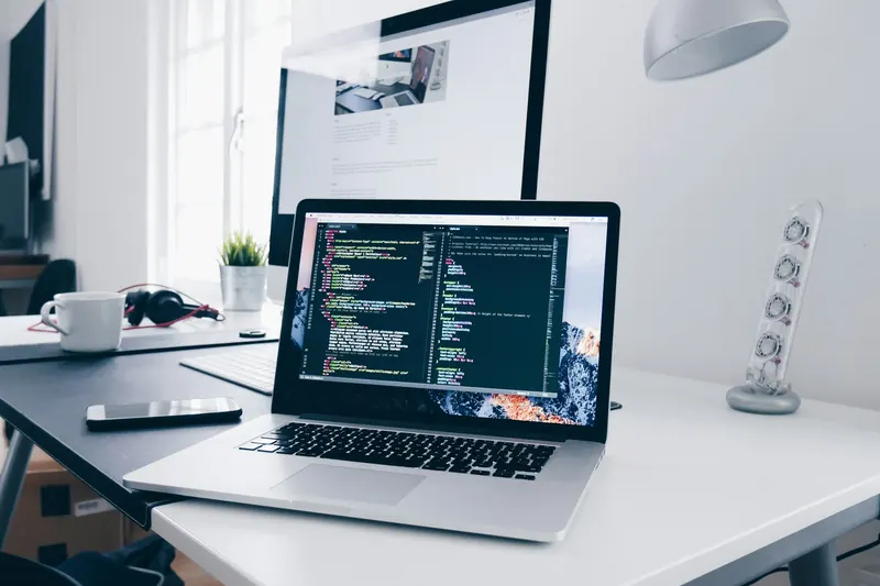 Laptop showing code beside a window in a bright workspace